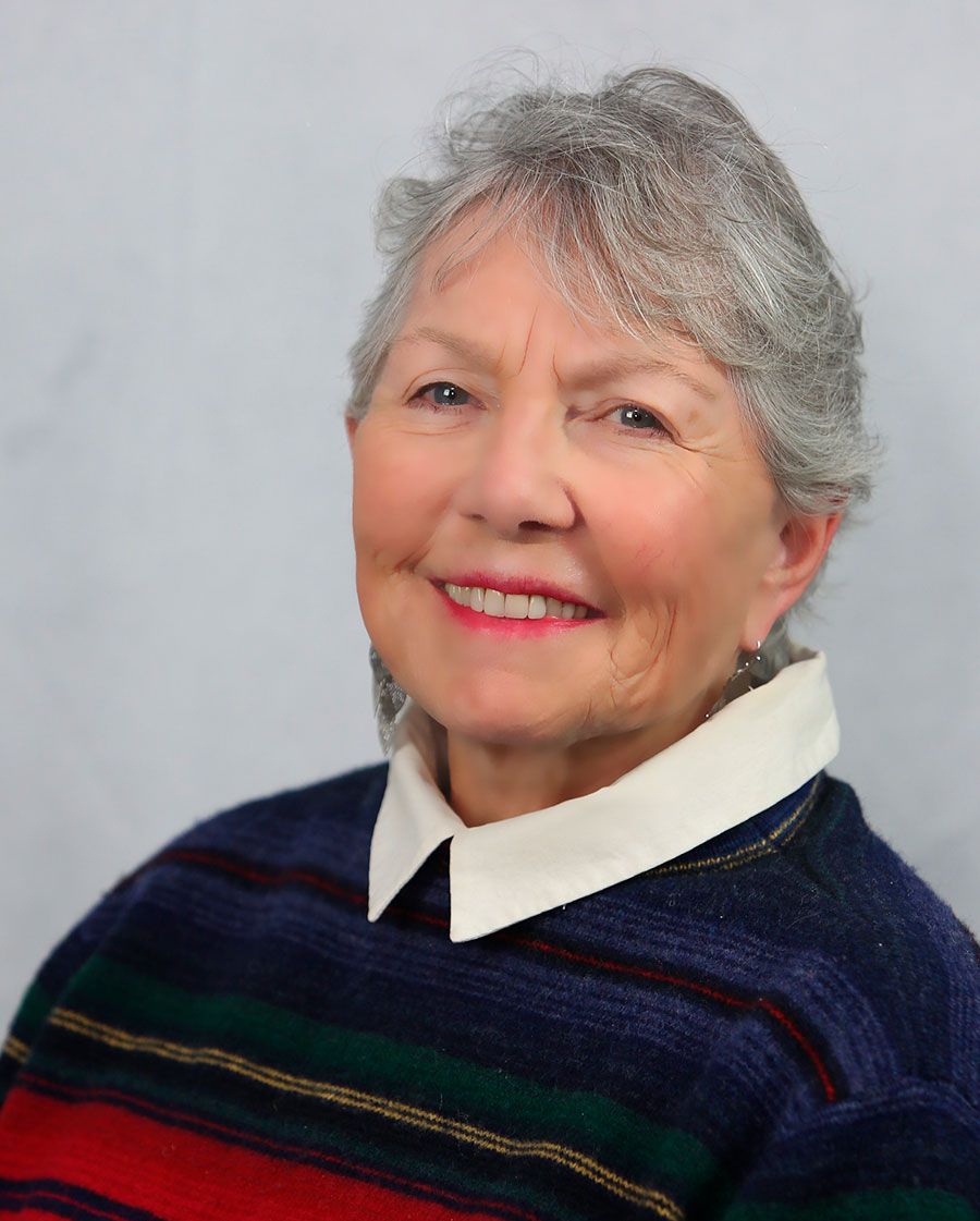 smiling portrait of catherine. she has short gray hair and is wearing a striped sweater with a white collared shirt