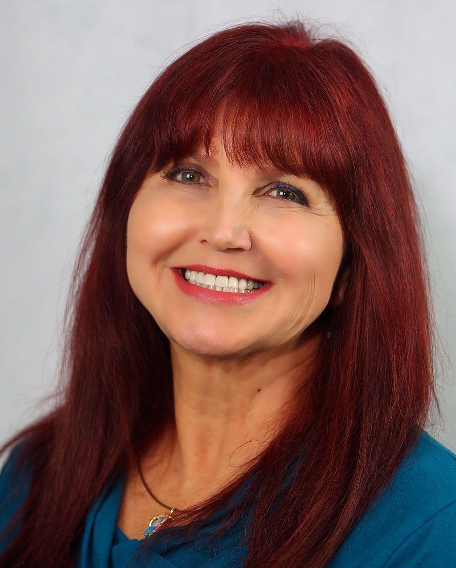 smiling portrait of diane. she has long auburn hair and is wearing a teal blouse