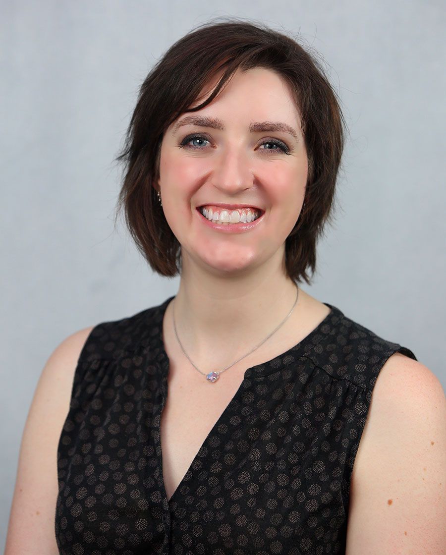 smiling portrait of stephanie. she has short brown hair and is wearing a black sleeveless blouse with gray dots